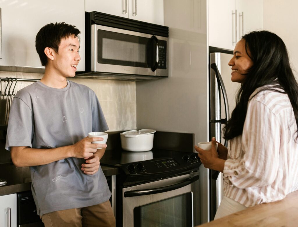 A man and a woman chatting happily while holding coffee cups in a modern kitchen.