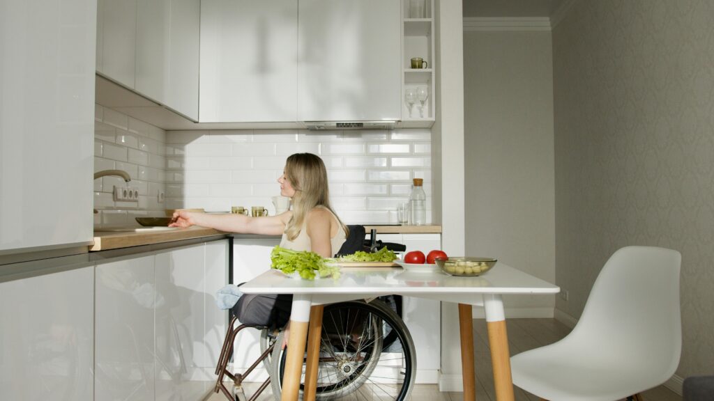 Woman in wheelchair preparing food in a modern kitchen with fresh vegetables.